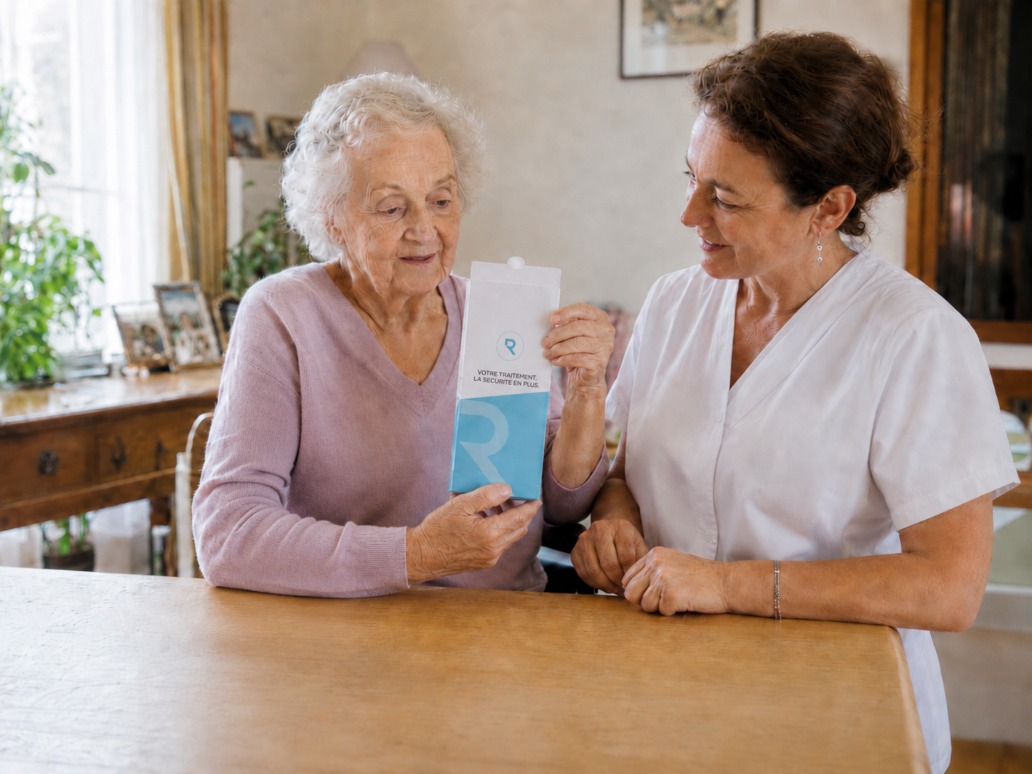 Patient âgé à domicile utilisant le pilulier Mon Oreus avec l'aide de son infirmière libérale pour améliorer l'observance médicamenteuse